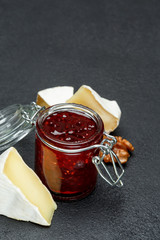 Jam of raspberries and pieces of brie cheese on dark concrete backround