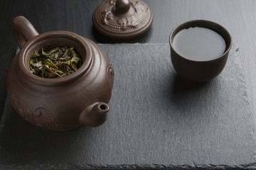 Obraz na płótnie Canvas Clay teapot with clay cup full of green tea on black slate background