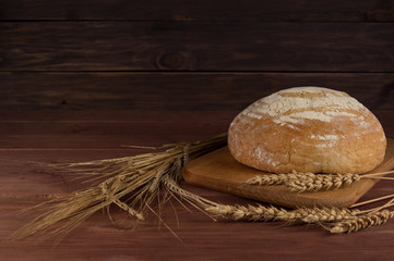 Freshly baked traditional bread with wheat on wooden background.
