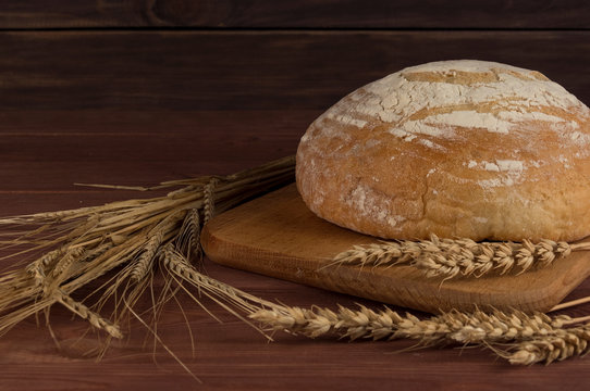 Freshly baked traditional bread with wheat on wooden background.