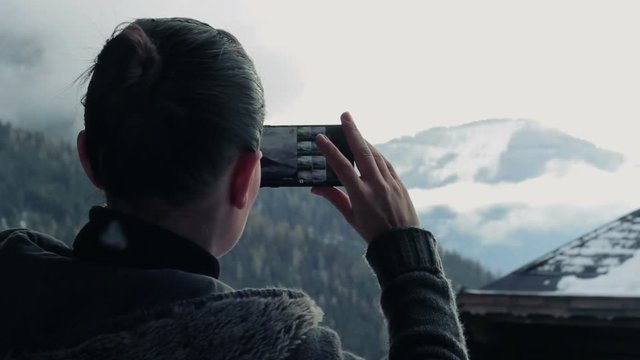 Young woman uses a smartphone to take a picture of beautiful view in the mountains, rear view