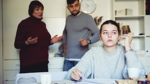 Frustrated young woman looking at papers on background with discontented husband and his mother