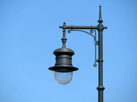 Decorated street lamp on the background of clear blue sky. Metal streetlight isolated, ornamented lantern