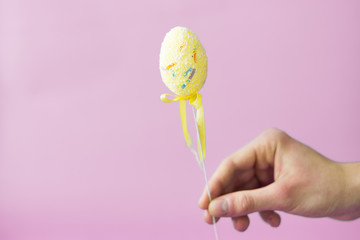 Man holding a yellow easter egg on a stick on a pink background