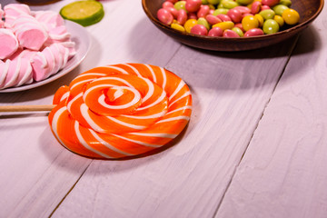 Ceramic plate with colored candies, lollipops and marshmallows on a wooden table