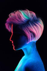Naklejka premium Model young beautiful girl portrait in studio, makeup, neon colors, ultraviolet lamp, color make-up, creative. Glows in the dark. Hair coloring with neon paints. Body art is blue, green, orange.