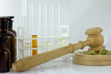 Obraz na płótnie Canvas Cannabis oil with apothecary jar and wooden judge hammer with sound block on the white mirror background - legal and illegal cannabis.