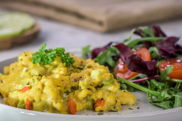 Scrambled eggs with pepper, avocado and parsley with saladdade witch eco spinach and rucola - close up.