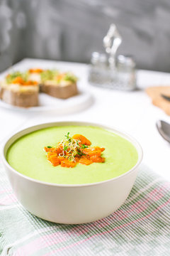Bowl of Green peas cream soup with baked carrot and microgreen sprouts on the served white wooden table. Healthy food, vegitarian diet concept. Selective focus, space for text.