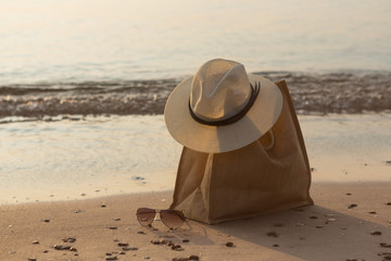 a female summer hat rests on a bag on the seashore, on the sand, early morning, the concept