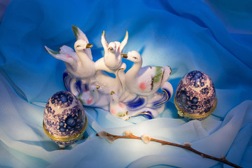 Figurines of birds with chicks,  easter eggs, willow branch on blue fabric 