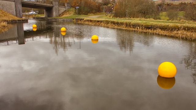 Bright yellow buoys with reflections on the surface of a canal.