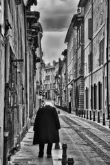 Fototapeta na wymiar Black and white vertical photo of a lone person on a small French street, neither the buildings nor the person are recognizable