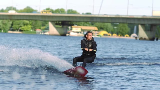 Wakeboarder jumping high above water. Professional sportsman making trick aver water surface. Athlete satisfied with his action. Young manwakeboarding on lake. Water sports. Extreme lifestyle