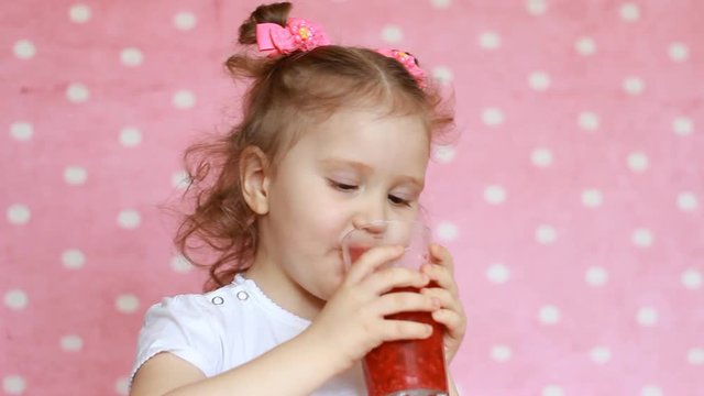 Happy cute little girl drinks raspberry smoothie and smiles. Vegetarian drink. Close-up portrait of a child who enjoys a refreshing tasty raspberry juice. Pink background