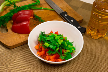 Preparation of a vegetarian salad with tomatoes, cucumbers, pepper and greens, seasoned with oil. Healthy food.