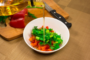 Preparation of a vegetarian salad with tomatoes, cucumbers, pepper and greens, seasoned with oil. Healthy food.