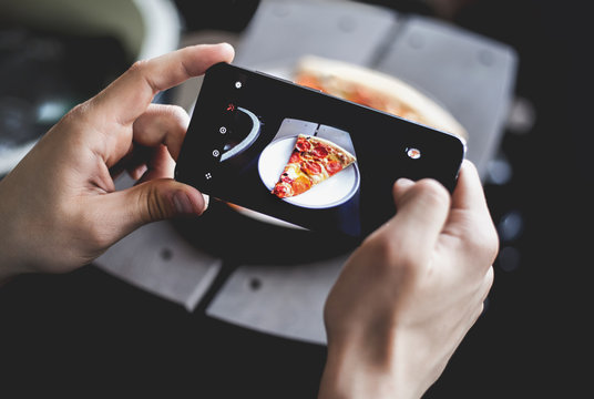 A young man taking photo of pizza on smartphone, photographing meal with mobile camera. Top view