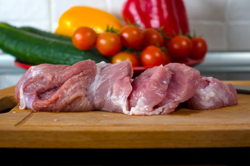A fresh piece of meat on a cutting board. Vegetables in background. Healthy food.