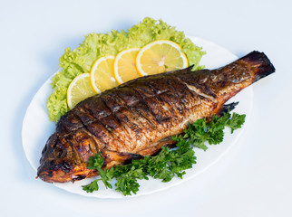 Fish cooked on fire on a white plate with lettuce leaves and parsley with lemon. restaurant supply