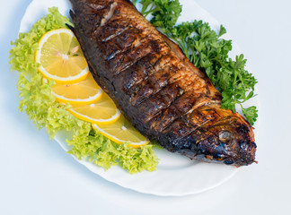 Fish cooked on fire on a white plate with lettuce leaves and parsley with lemon. restaurant supply