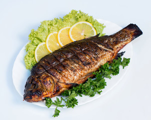 Fish cooked on fire on a white plate with lettuce leaves and parsley with lemon. restaurant supply