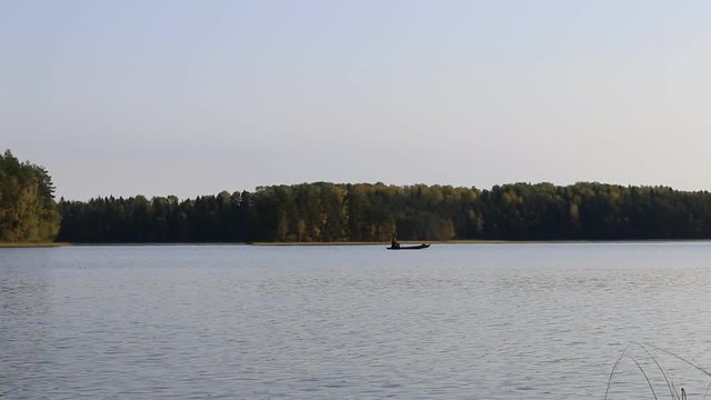 Waterman sails by old canoe on forest lake. Boats are traditionally used for fishing and ferry. North Russia, Vepsian Karelia
