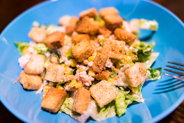 Macro closeup of homemade ceasar salad on blue plate, wooden table, fork, croutons, lettuce background