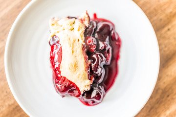 Closeup of hot fresh red cherry cobbler slice piece on white plate on table golden crust, gooey thick filling flat top