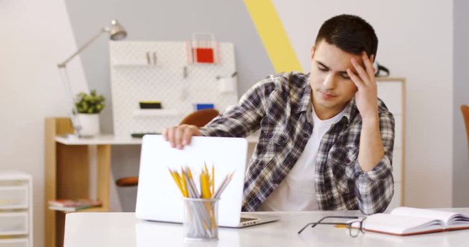 Tired young caucasian man working on the laptop computer in the modern ofice, then lying his head on the table and sleeping. Inside