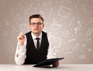 Young handsome businessman sitting at a desk with white mixed media icons behind him