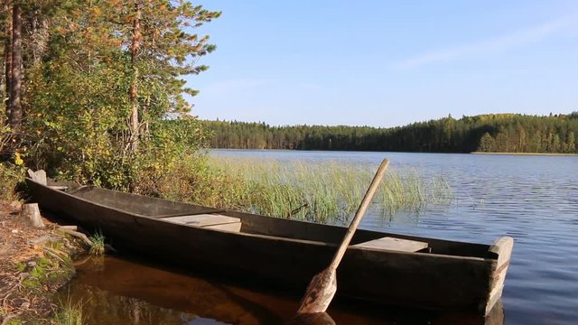 Wooden homemade boat (punt) with sliced oar on forest lake. Boats are traditionally used for fishing with light at night and nets. North Russia, Vepsian Karelia
