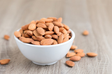 Pile of almonds nut in a while bowl against wooden background select focus shallow depth of field