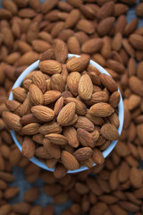 Pile of almonds nut in a while bowl against dark rustic wooden background select focus shallow depth of field
