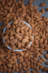 Pile of almonds nut in a while bowl against dark rustic wooden background select focus shallow depth of field