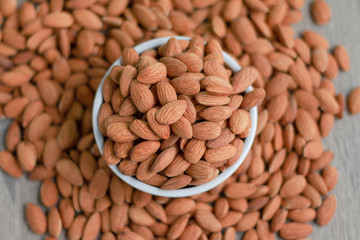 Pile of almonds nut in a while bowl against wooden background select focus shallow depth of field