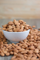 Pile of almonds nut in a while bowl against wooden background select focus shallow depth of fieldPile of almonds nut in a while bowl against wooden background select focus shallow depth of field