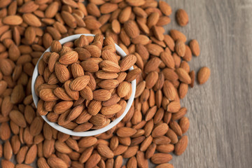 Pile of almonds nut in a while bowl against wooden background select focus shallow depth of field