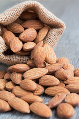 Pile of almonds nut in sackcloth bag against wooden background select focus shallow depth of field