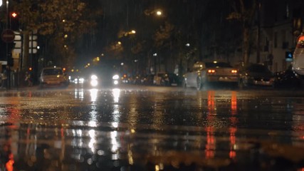 PARIS, FRANCE - SEPTEMBER 29, 2017: Slow motion shot of rain pouring in the street and making puddles, cars driving in night city