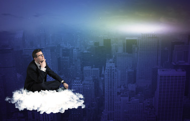 Fototapeta premium Caucasian businessman sitting on a white fluffy cloud above the city, thinking and wondering