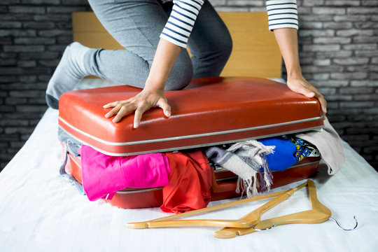 Travel and vacation concept, happiness woman packing stuff and a lot of clothes into suitcase on bed prepare for her travel and journey trip