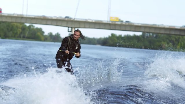 Joyful man wakeboarding on city river. Extreme entertainment on water. Athlete moving fast on water ski on water. Extreme water sports. Active rest in nature. Extreme summer activity