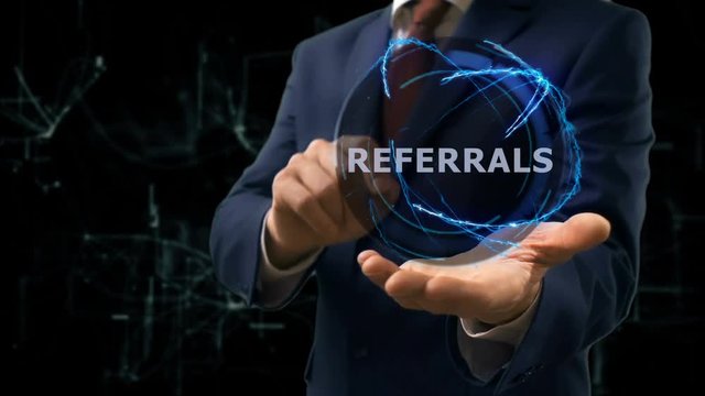 Businessman shows concept hologram Referrals on his hand. Man in business suit with future technology screen and modern cosmic background