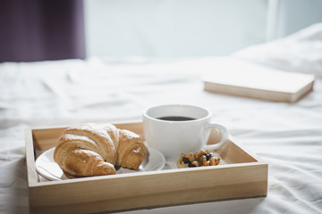 Morning cup of coffee and Croissant on the bed with old book