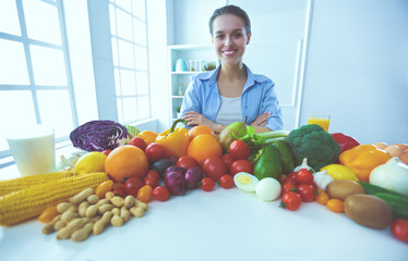 Young and cute woman sitting at the table full of fruits and vegetables in the wooden interior