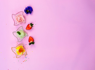 Ice cream in wave glass bowls with edible flowers *pansy, violet( on pink background. Pink (strawberry), yellow (mango or banana) and green (lime, green tea or pistachio). Top view