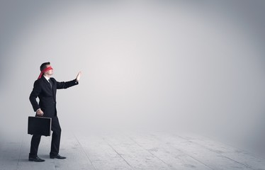 A young male business person in elegant dress standing with red blindfolds in a clear, empty space concept.