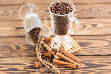 Lot of fried coffee beans in transparent glass for mulled wine on pallet near anise and threads and three cinnamon sticks and coffee beans poured out of glass on old wooden rustic brown table