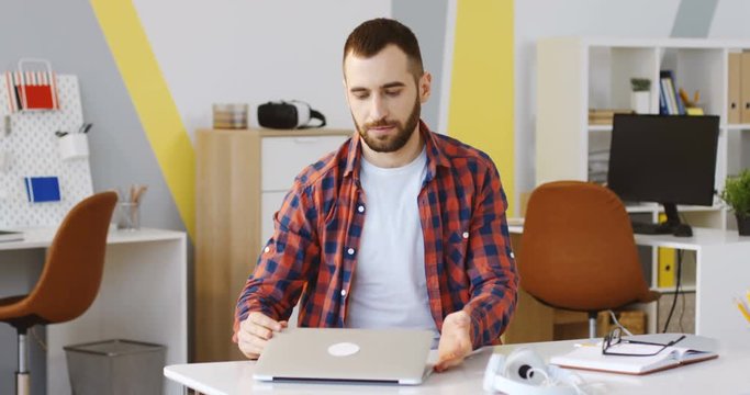Caucasian male office worker shutting down his laptop computer and crossing his hands for praying or meditating in the cozy office room. Indoors